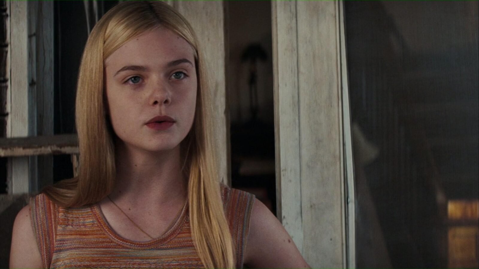 Elle Fanning, atriz mirim, em trecho de filme, sentada e olhando atentamente para frente. 