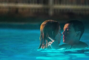 Em uma piscina, uma mulher e um homem estão abraçados e com rostos próximos.