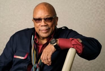 Quincy Jones com o braço apoiado em uma cadeira.