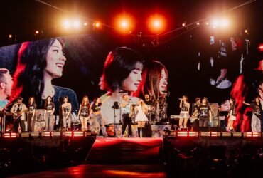 A banda Coldplay, que possui quatro integrantes, canta em seu show junto do grupo Twice, que possui nove integrantes. Todos aparecem sorridentes, enfileirados lado a lado.