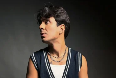 O cantor PeLu está olhando para o lado direito da imagem com uma expressão relaxada.