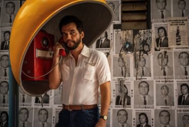 O ator Wagner Moura aparece usando um telefone público em foto de divulgação do filme O Agente Secreto