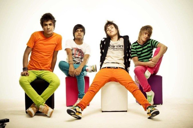 Os quatro integrantes da banda restart aparecem sentados em bancos do tipo puff. Eles vestem roupas coloridas em contraste com o cenário branco. 