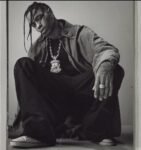 O Rapper Travis Scott, atração do festival The Town 2025, posa para foto. O artista é um jovem homem negro com tranças no cabelo. Ele possui uma tatuagem na mão esquerda e veste roupas largas.