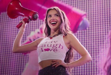 Olivia rodrigo sorri enquanto segura um megafone durante um show