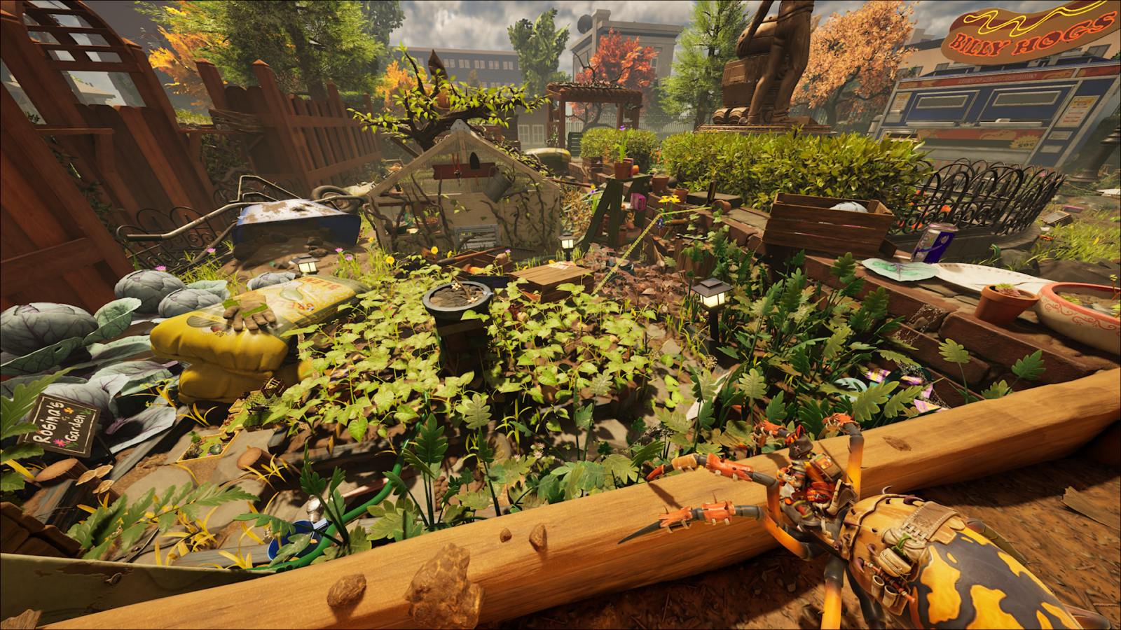 Perspectiva da montaria, mostrando um jardim detalhado em escala minúscula. O cenário inclui canteiros de plantas, um saco de fertilizante amarelo, cercas de madeira e, ao fundo, estruturas maiores como uma estátua e um carrinho de comida "Billy Hogs" sob um céu nublado.