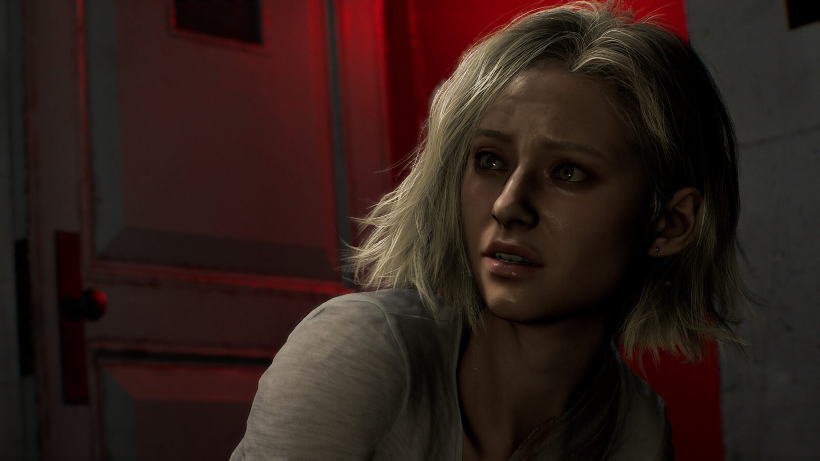 Grace Ashcroft, uma jovem mulher de cabelos loiros curtos e desalinhados, com expressão de medo e incerteza. Ela olha para o lado em um ambiente sombrio, iluminado por uma luz vermelha intensa que vem de uma porta ao fundo, sugerindo perigo iminente.