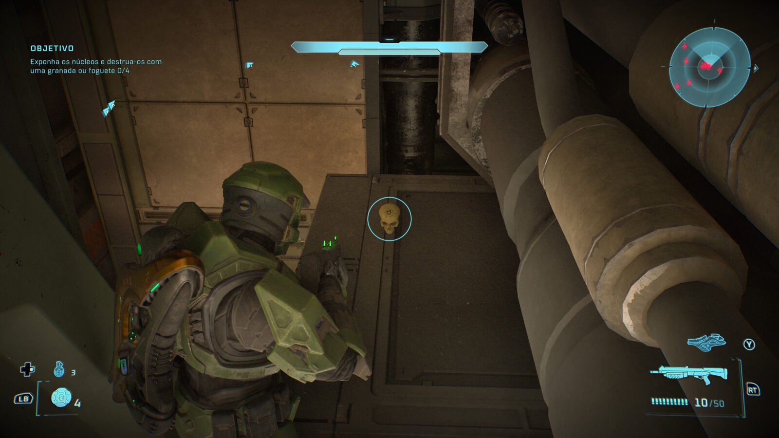Perspectiva de terceira pessoa do Master Chief, utilizando sua armadura verde em um ambiente industrial alienígena de metal, com tubos grandes à direita. O Spartan está olhando para um crânio alienígena colecionável que está destacado por um círculo ciano em uma passarela de metal à frente. O HUD do jogo é visível no topo e no canto inferior esquerdo.