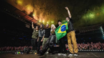 ​Foto do Linkin Park no palco do Allianz Parque em 2024. A banda posa com a bandeira do Brasil diante de uma multidão e fogos de artifício.