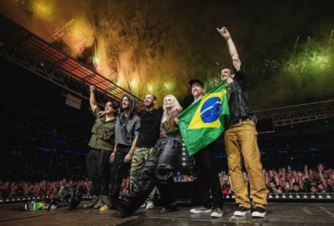 ​Foto do Linkin Park no palco do Allianz Parque em 2024. A banda posa com a bandeira do Brasil diante de uma multidão e fogos de artifício.