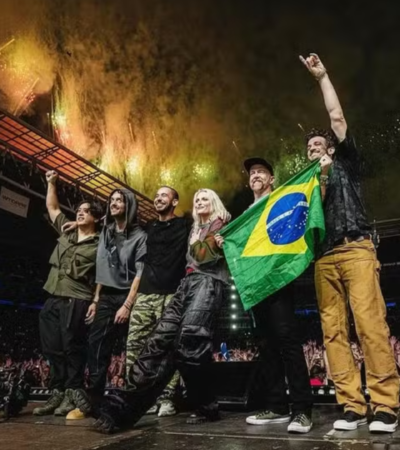 ​Foto do Linkin Park no palco do Allianz Parque em 2024. A banda posa com a bandeira do Brasil diante de uma multidão e fogos de artifício.