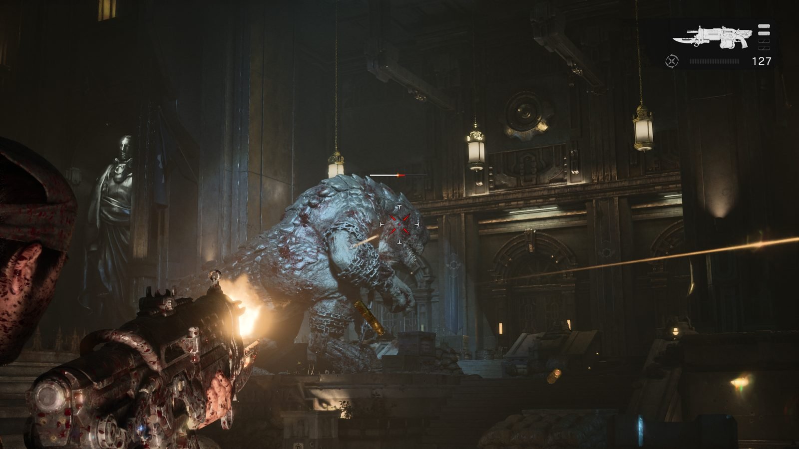 Uma captura de tela de Gears of War: E-Day, de uma perspectiva de terceira pessoa com uma arma robusta e cheia de cicatrizes de batalha, dispara um flash de luz contra um colossal monstro Berserker bípede e blindado. O monstro está no centro de um grande e sombrio salão de catedral gótica, com estátuas e arcos de pedra. O HUD mostra 127 de munição no canto superior direito, e uma cápsula de munição cai no meio.