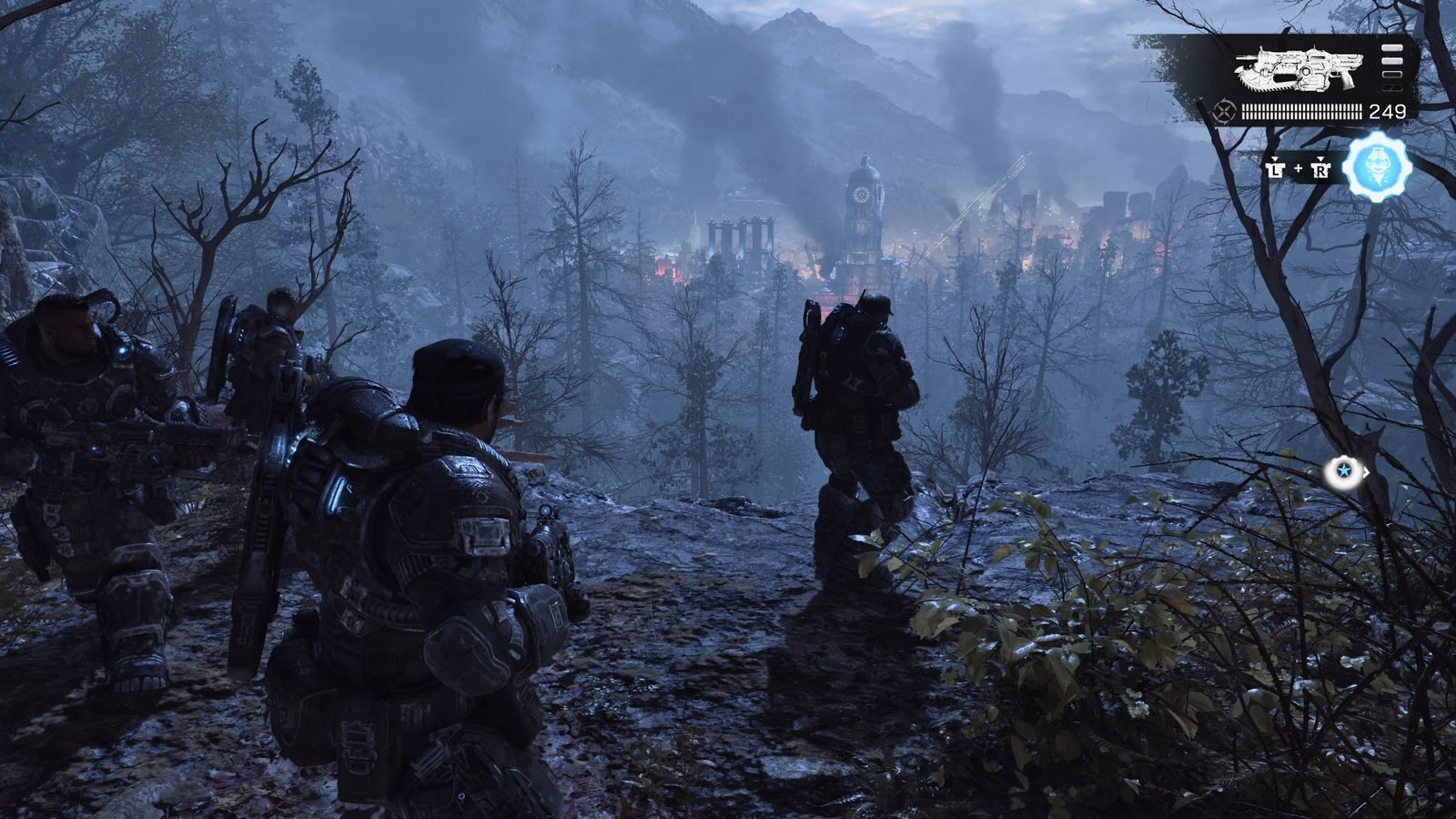 Uma captura de tela de Gears of War: E-Day mostrando o esquadrão Bravo observando de um penhasco uma cidade distante em chamas, cercada por fumaça e montanhas cobertas de árvores escuras ao anoitecer.